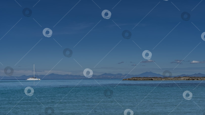 Скачать Идиллический морской пейзаж. В спокойном синем океане видна белая яхта с высокой мачтой. фотосток Ozero