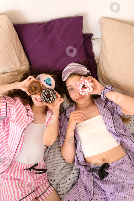 Скачать Девушки в полосатых пижамах наслаждаются пончиками во время игривой вечеринки с ночевкой. фотосток Ozero
