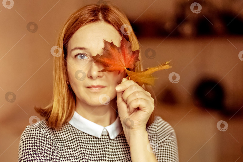 Скачать Портрет молодой женщины, прикрывающей один глаз осенним опавшим кленовым листом. Осеннее настроение фотосток Ozero