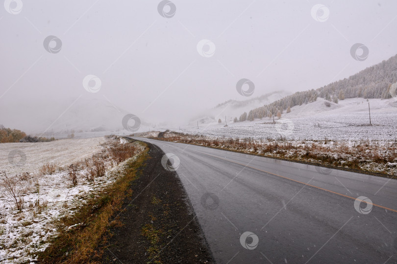 Скачать Асфальтированная дорога, идущая через горную долину, покрытую первым снегом. фотосток Ozero