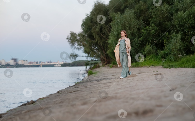 Скачать Молодая красивая кавказка, счастливо улыбающаяся, наслаждается прогулкой по набережной. Портрет женщины в джинсах и бежевом плаще. фотосток Ozero