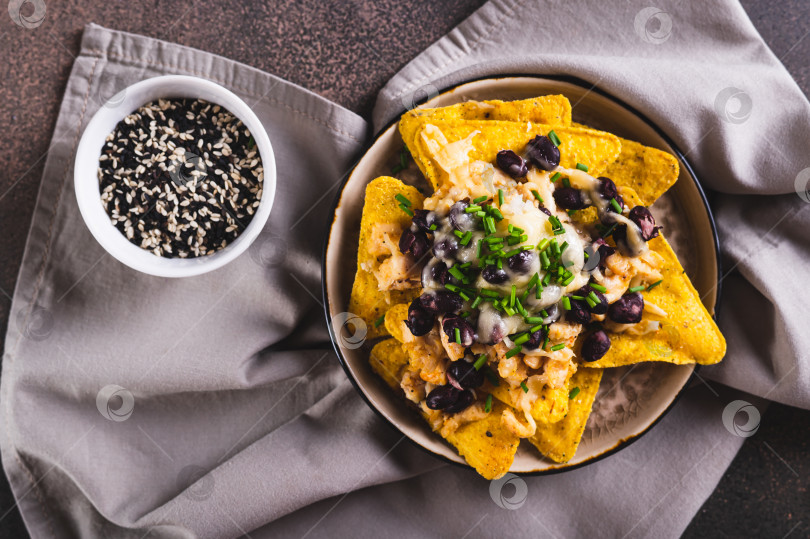 Скачать Мексиканские чипсы начо, запеченные с курицей, черной фасолью и сыром, крупным планом на тарелке, вид сверху фотосток Ozero