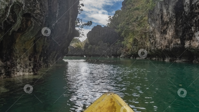 Скачать Каноэ плывет по живописной изумрудной тропической лагуне, окруженной отвесными карстовыми скалами. фотосток Ozero