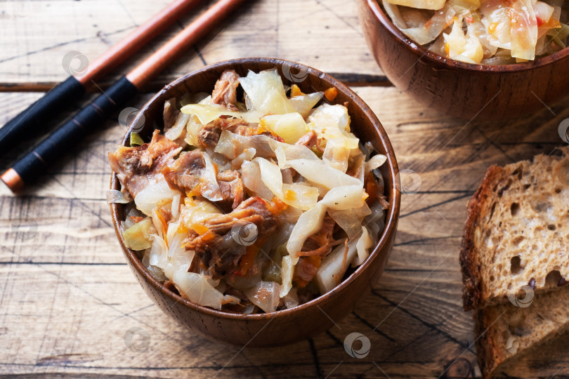 Скачать Тушеная капуста с мясом в деревянной посуде на деревянном фоне. Традиционное русское блюдо - солянка. фотосток Ozero