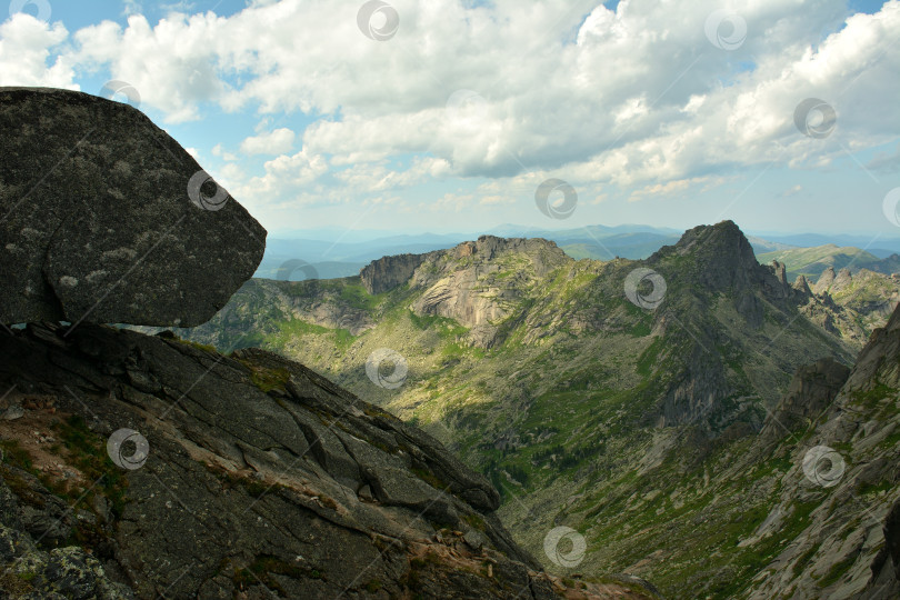 Скачать Большой каменный валун на краю высокого обрыва, возвышающегося над горным хребтом в солнечный летний день. фотосток Ozero