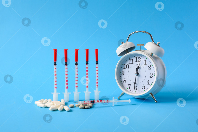 Скачать Несколько шприцев с инсулином рядом с будильником на синем фоне. Концепция планового лечения сахарного диабета. фотосток Ozero