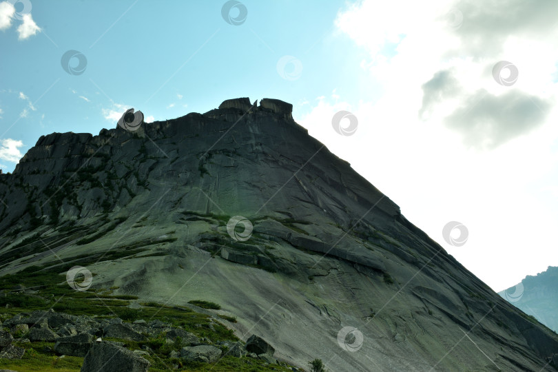 Скачать Высокий скалистый массив со скользкими краями и заостренной вершиной на фоне яркого облачного неба летним вечером. фотосток Ozero