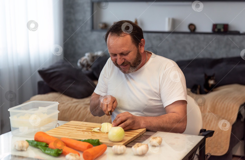 Скачать Зрелый мужчина готовит плов, режет овощи на кухне у себя дома фотосток Ozero