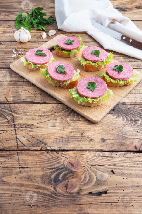 Скачать Бутерброды с листьями салата и нарезанной колбасой салями на деревянной доске. вид сверху фотосток Ozero