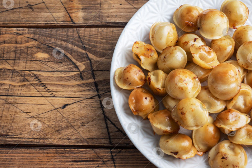 Скачать Традиционные жареные пельмени, равиоли, вареники с мясной начинкой на тарелке, русская кухня. Деревянный стол в деревенском стиле, место для копирования. фотосток Ozero