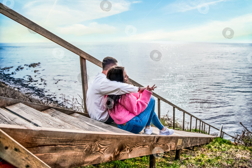 Скачать Молодая супружеская пара сидит на длинной деревянной лестнице и смотрит на Японское море фотосток Ozero