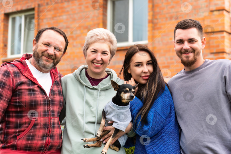 Скачать Портрет счастливой семьи, обнимающейся с собакой возле своего дома. фотосток Ozero