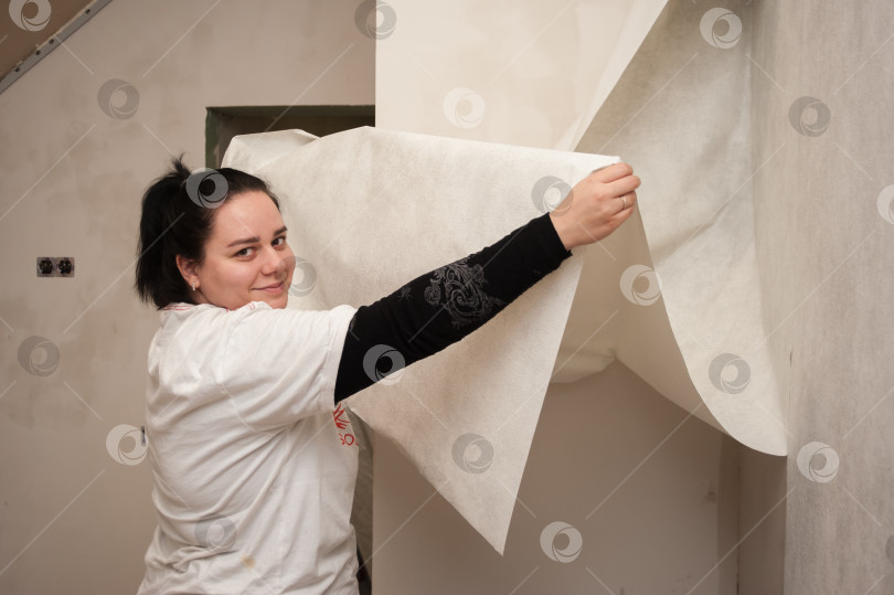 Скачать Молодая семья, парень и девушка, вместе делают ремонт, клеят обои и красят стены фотосток Ozero