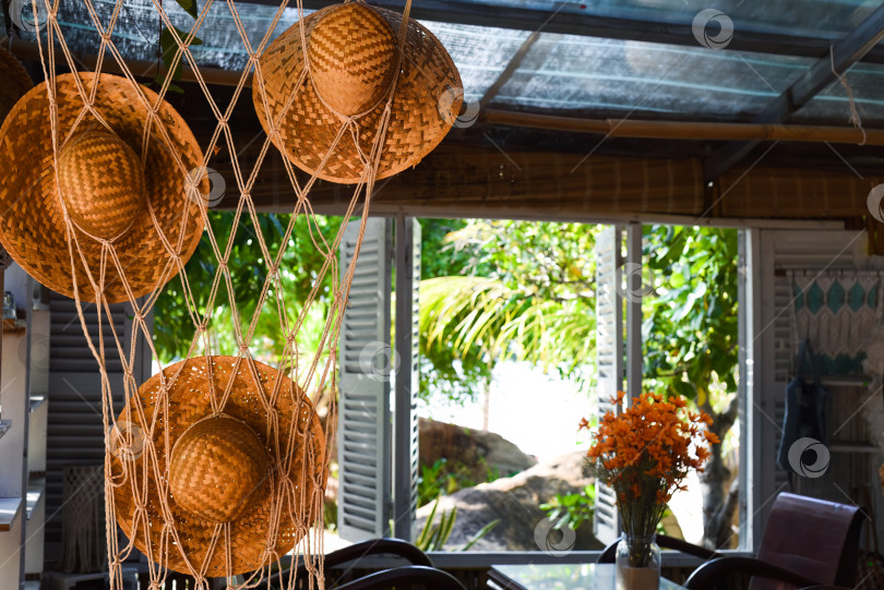 Скачать Оранжевые соломенные шляпы, висящие рядом с открытыми окнами, и букет цветов в летний день фотосток Ozero