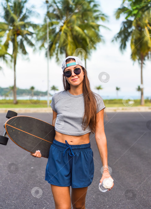 Скачать Молодая красивая женщина в кепке стоит и держит в руках скейтборд с невозмутимым лицом фотосток Ozero