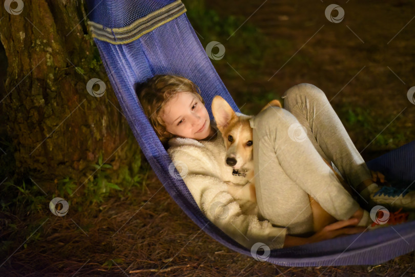 Скачать Симпатичная маленькая девочка спит в гамаке и держит на руках собаку корги во время похода фотосток Ozero