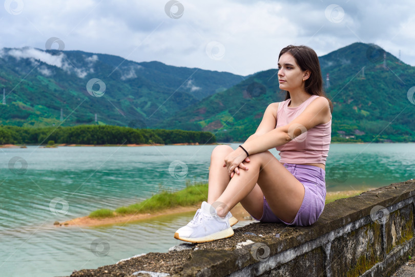Скачать Молодая русская женщина сидит с подавленным и печальным лицом на фоне озера и гор в провинции Кханьхоа, Вьетнам фотосток Ozero