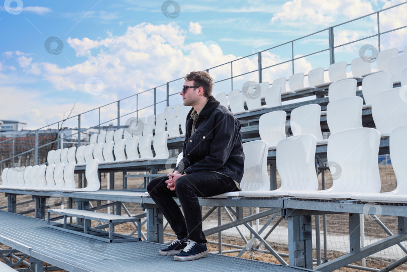 Скачать Один молодой человек сидит на пустой футбольной трибуне на улице фотосток Ozero
