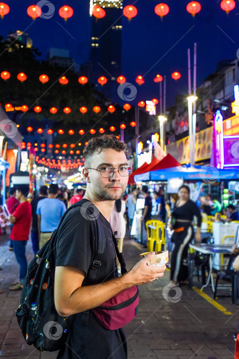 Скачать Молодой турист ест мороженое на улице Джалан Алор в Куала-Лумпуре, Малайзия фотосток Ozero