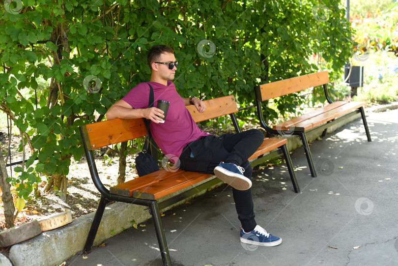 Скачать Молодой русский мужчина с чашкой кофе отдыхает на скамейке фотосток Ozero