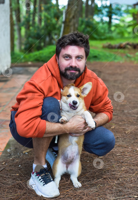 Скачать Молодой бородатый мужчина играет со своей собакой корги утром в лесу фотосток Ozero