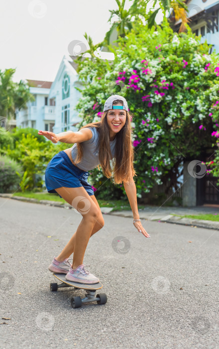 Скачать Молодая красивая женщина в кепке катается на скейтборде и смеется фотосток Ozero