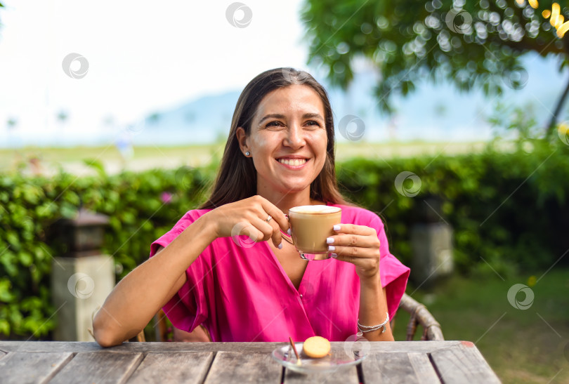 Скачать Портрет улыбающейся русской женщины, пьющей горячий капучино и смотрящей налево фотосток Ozero