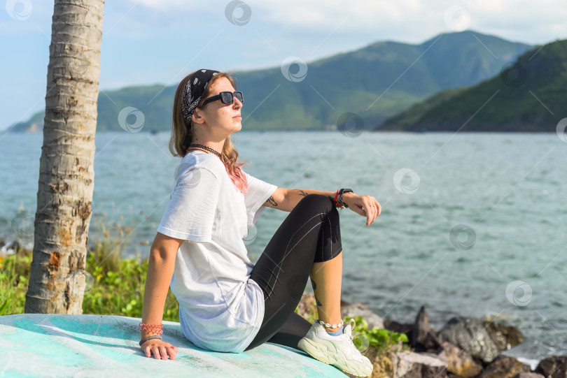 Скачать Молодая путешественница в темных очках и бандане сидит на берегу Южно-Китайского моря во Вьетнаме фотосток Ozero