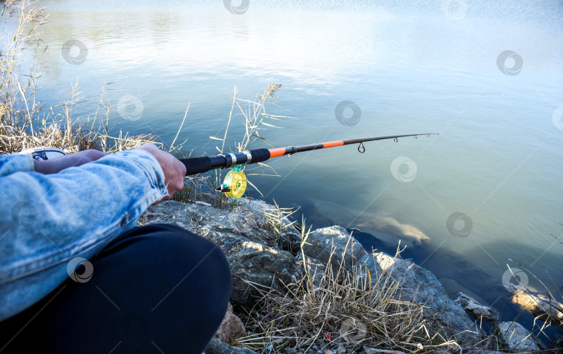 Скачать Удочка с поплавком и катушкой в руках рыбака на фоне озера осенним вечером. фотосток Ozero