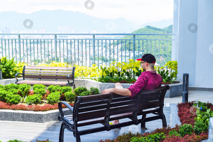Скачать Молодой турист отдыхает на скамейке и смотрит на город Нячанг фотосток Ozero