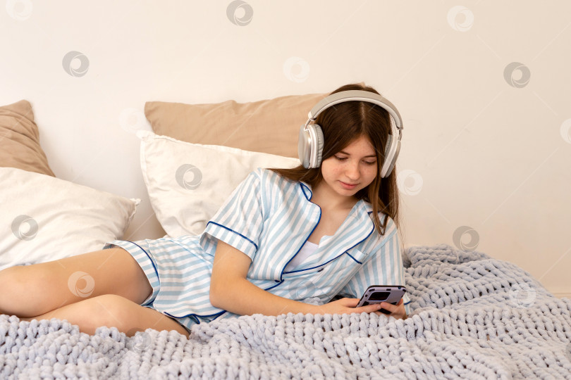 Скачать Девочка-подросток лежит на кровати, используя смартфон и наушники фотосток Ozero