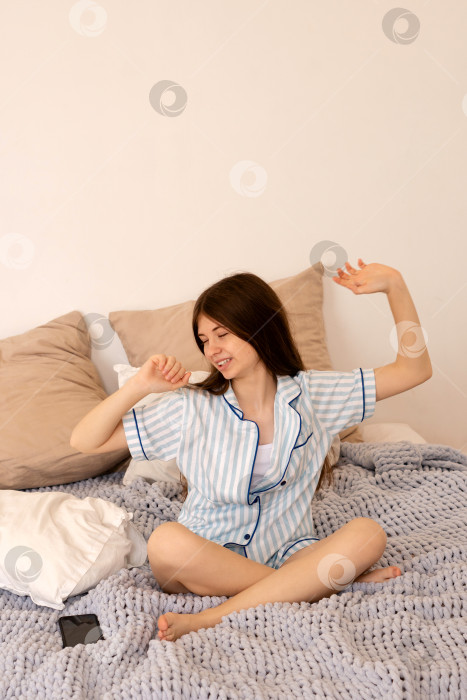 Скачать Девочка-подросток потягивается и улыбается, сидя на кровати. фотосток Ozero