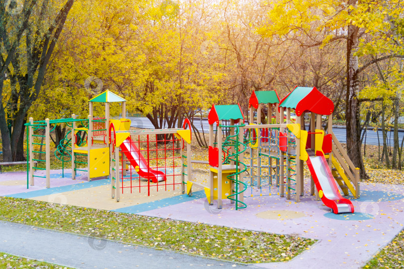 Скачать Вид на разноцветную игровую площадку в осеннем парке, освещенную солнечным светом фотосток Ozero