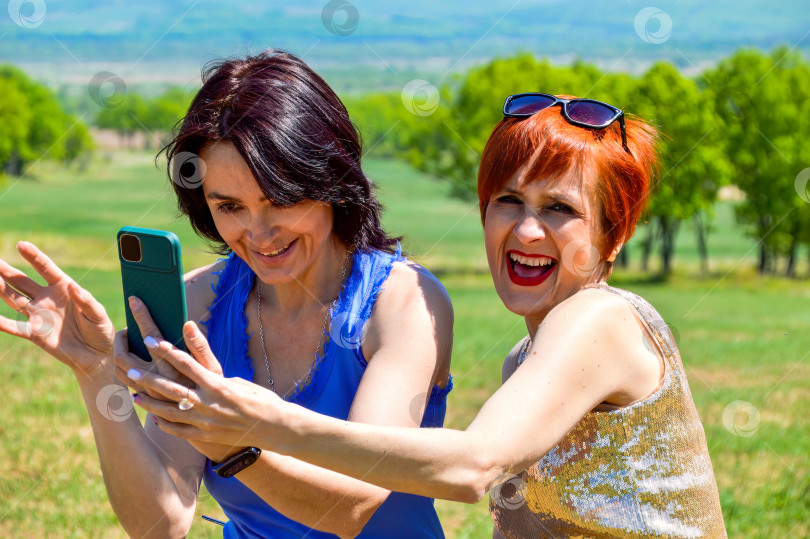 Скачать Две сестры держат в руках телефон, чтобы сделать селфи-фото. Они искренне смеются, обнажая зубы фотосток Ozero