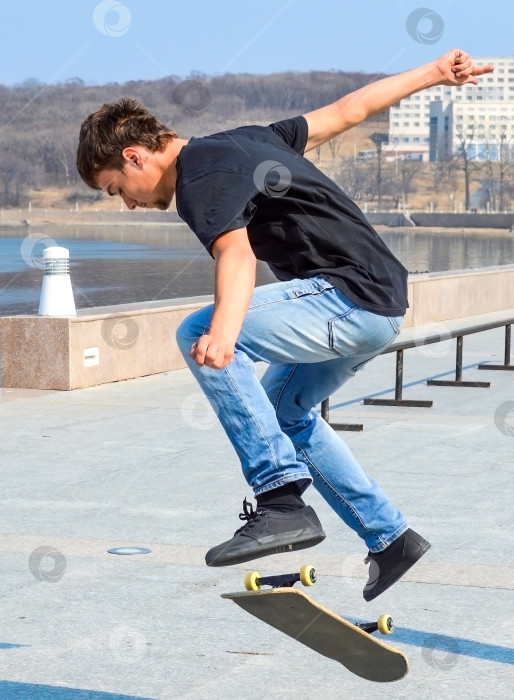 Скачать Молодой русский фигурист в черной футболке и синих джинсах прыгает на скейтборде ранним весенним днем фотосток Ozero