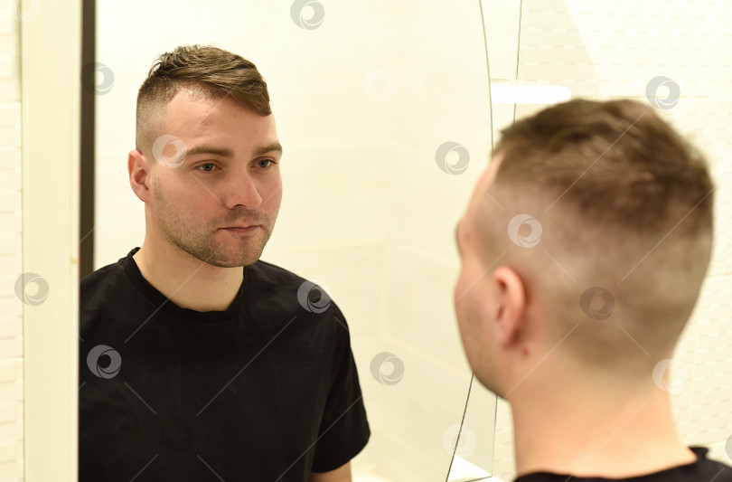 Скачать Молодой человек смотрит в зеркало на свое отражение в ванной комнате фотосток Ozero