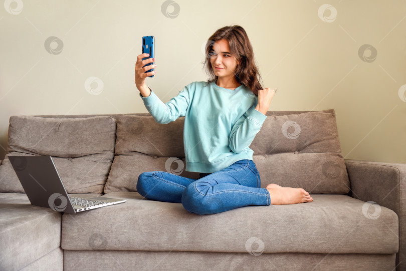 Скачать Молодая улыбающаяся женщина делает селфи для своего профиля. Она сидит дома на диване рядом с ноутбуком. карантин и концепция онлайн-знакомств фотосток Ozero