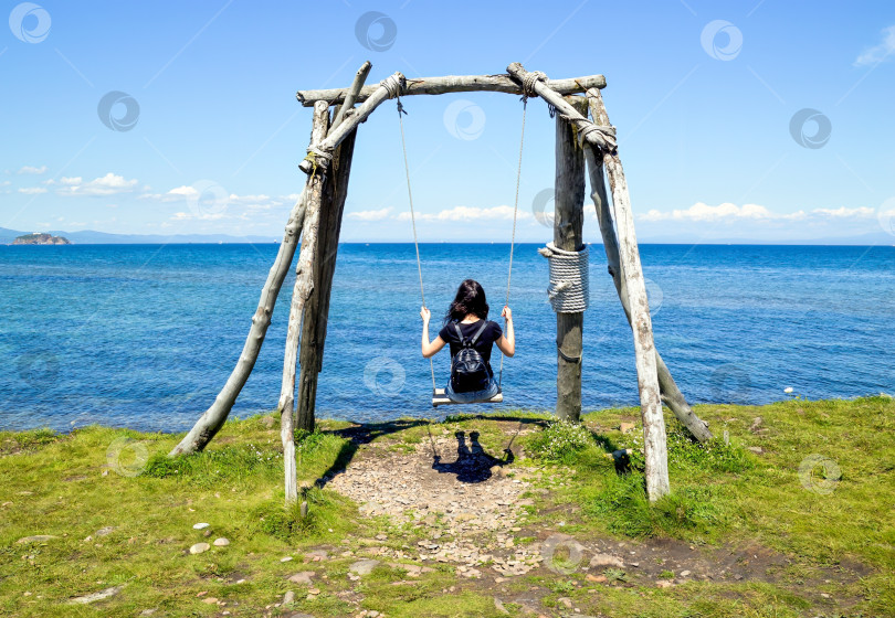 Скачать Молодая брюнетка сидит на деревянных качелях спиной к камере на фоне Японского моря летним днем фотосток Ozero