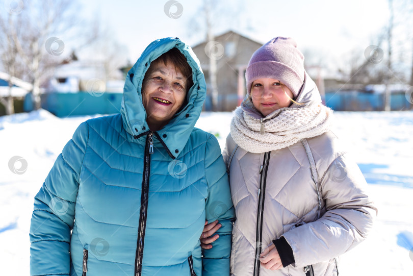 Скачать Портрет русской 12-летней девочки и ее бабушки, смотрящих в камеру на фоне зимы. фотосток Ozero