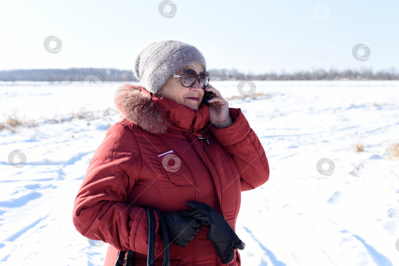 Скачать Русская пожилая женщина разговаривает по телефону на фоне заснеженного поля. зима фотосток Ozero