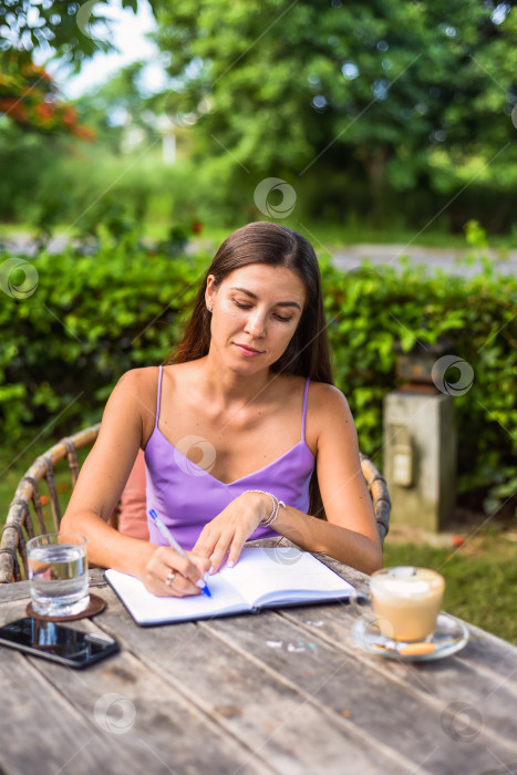 Скачать Симпатичная женщина сидит на стуле в летнем саду и пишет в блокноте фотосток Ozero
