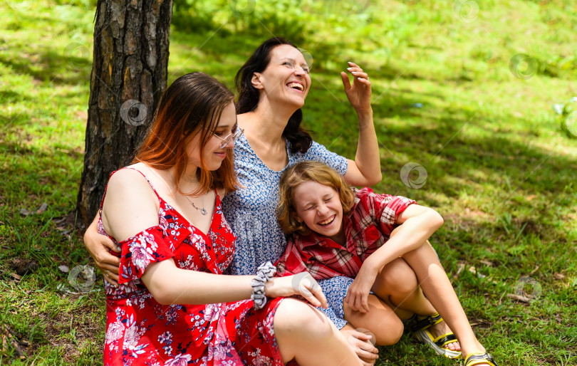 Скачать Мать обнимает свою дочь-подростка и маленькую дочурку и смеется вместе с ними в лесу фотосток Ozero