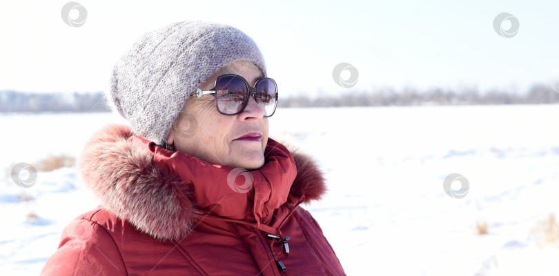 Скачать Портрет русской пожилой женщины в шапочке и солнцезащитных очках, смотрящей вдаль на фоне заснеженного поля. зима фотосток Ozero