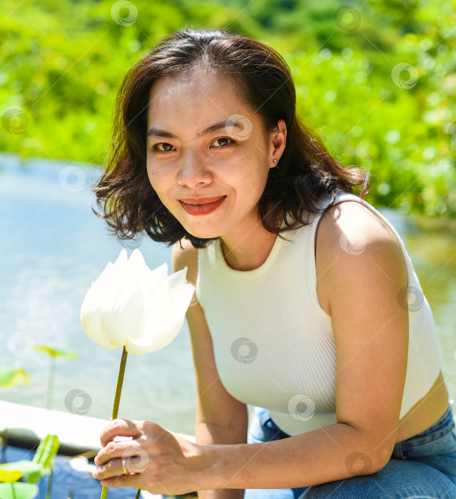 Скачать Молодая вьетнамская женщина улыбается и вдыхает запах белого лотоса во Вьетнаме фотосток Ozero
