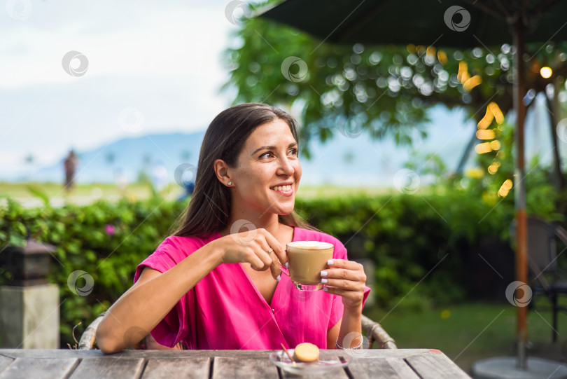 Скачать Портрет улыбающейся русской женщины, пьющей горячий капучино и смотрящей налево фотосток Ozero