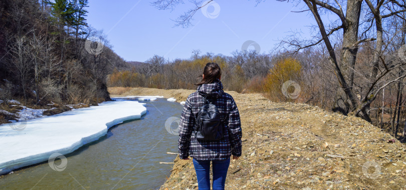 Скачать Молодая брюнетка отправляется в поход в лес рядом с тающей от снега рекой в весенний солнечный день. Одинокий путешественник фотосток Ozero