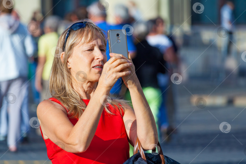 Скачать Москва, Россия, август 2018 года: Пожилая женщина фотографирует на телефон на фоне толпы туристов на Красной площади (редакционная статья) фотосток Ozero