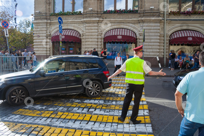 Скачать Москва, Россия, август 2018 г.: Мужчина в светло-зеленом защитном жилете регулирует движение на пешеходном переходе в центре города (редакционная статья) фотосток Ozero