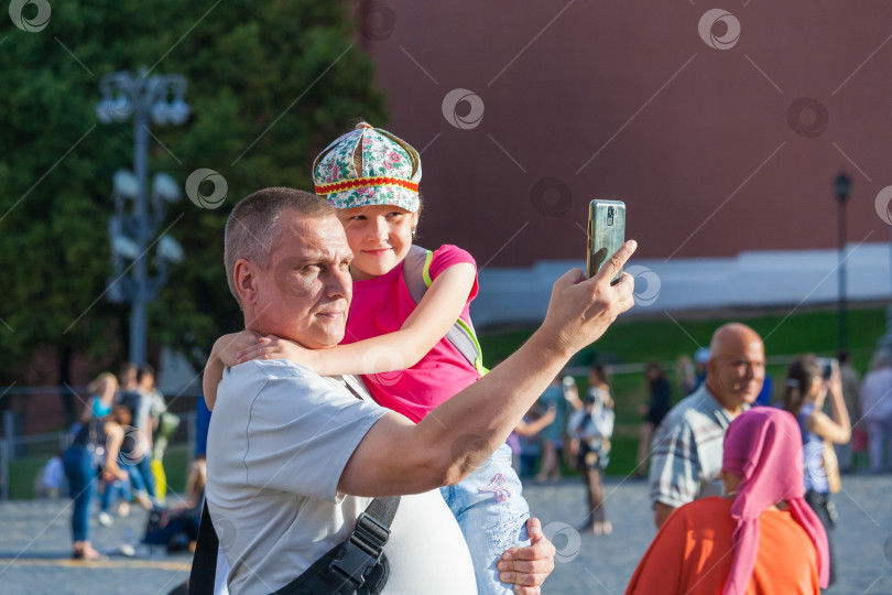 Скачать Москва, Россия, август 2018 года: Мужчина с ребенком делает селфи на фоне Красной площади с толпой туристов (редакционная статья) фотосток Ozero