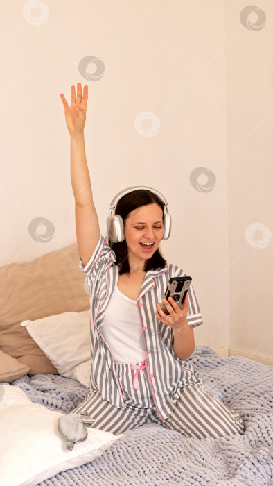 Скачать Женщина в наушниках празднует победу, подняв руку в постели. фотосток Ozero
